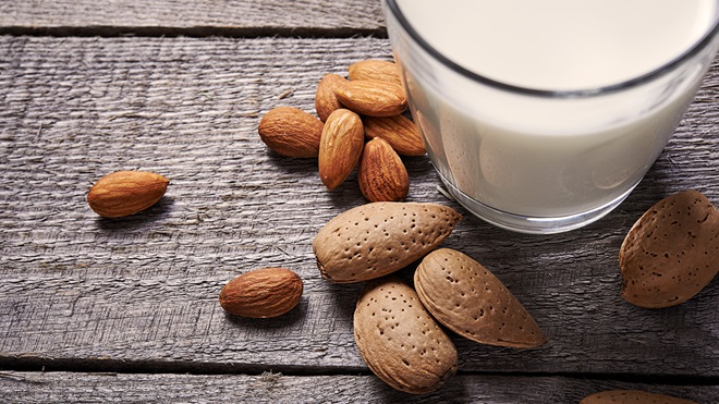 glass of almond milk surrounded by almonds